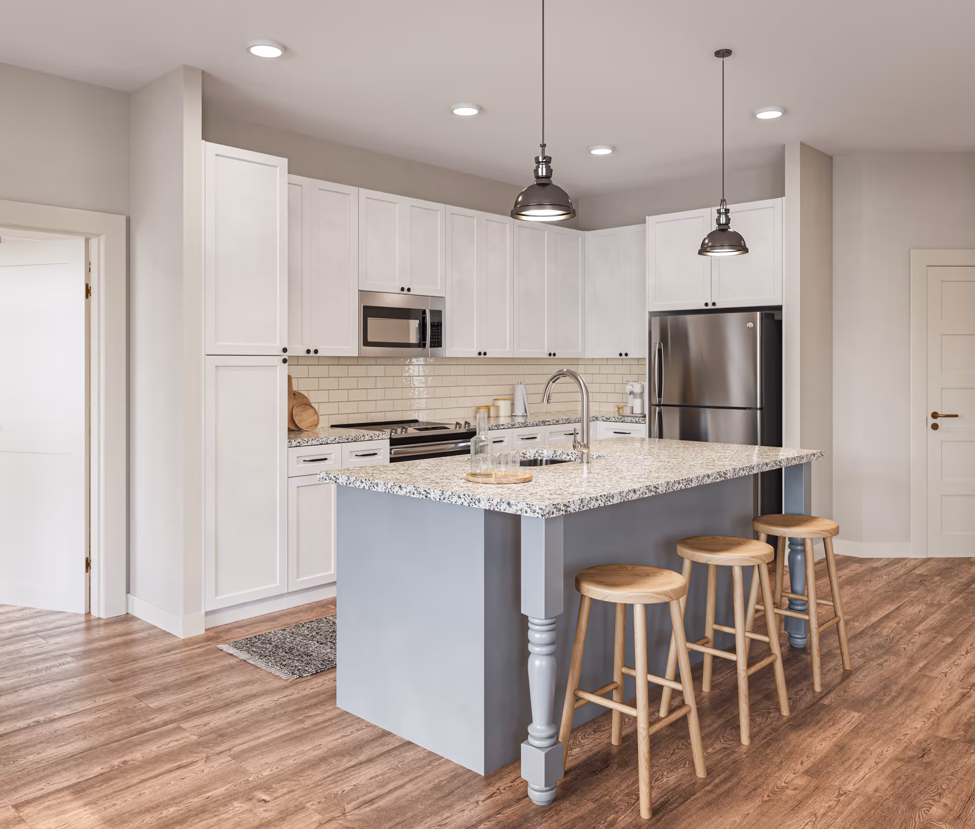 Modern kitchen with white cabinets, stainless steel appliances including a refrigerator and microwave, a large island with a speckled countertop, three wooden stools, and pendant lights hanging from the ceiling. The floor is wood with a light brown finish.