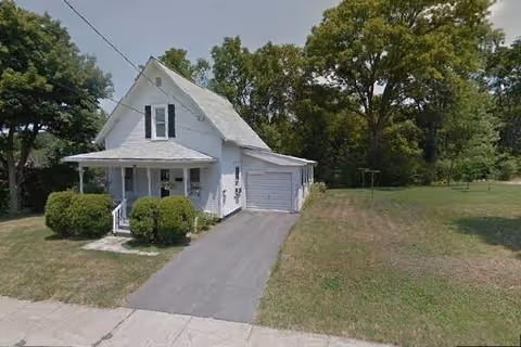 White, pitched-roof building with a small front porch, driveway, and surrounding lawn.