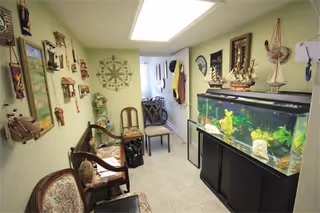 Narrow interior room with several chairs, wall decorations and a large aquarium on a cabinet.