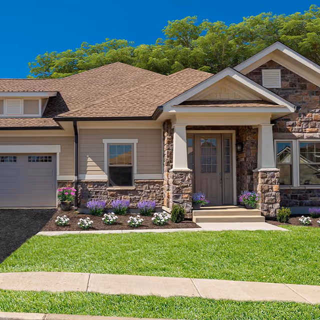 Front exterior of a single-story home with a stone-accented entrance, attached garage, manicured lawn and flower beds.