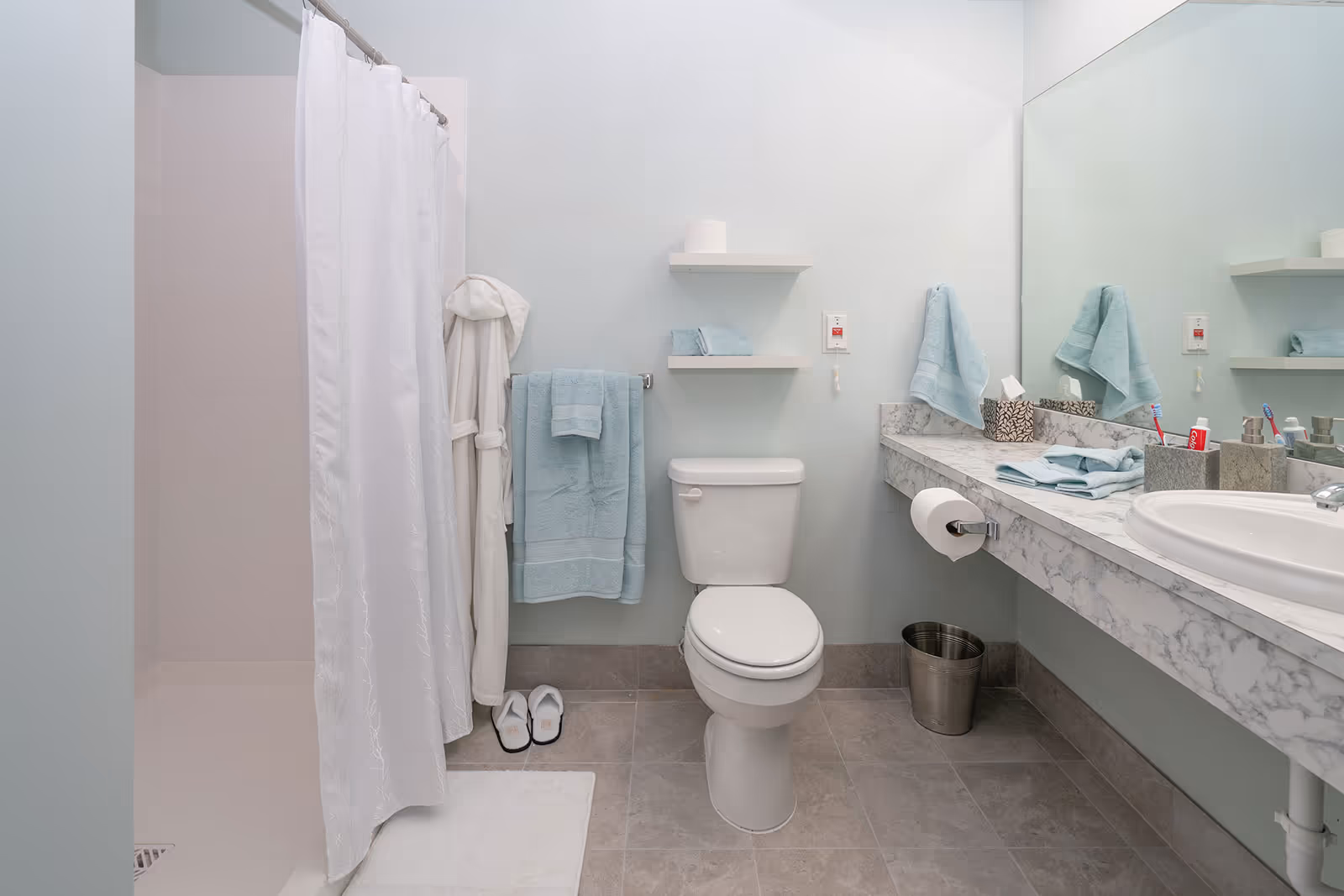 Blue bathroom featuring shower curtain, toilet, towels, and marble countertop.