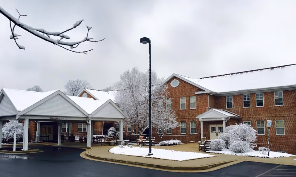 Exterior view of a two-story brick building with a covered entrance and snow-covered ground, trees, and bushes under an overcast sky.