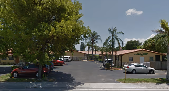 Exterior view of Apollo Gardens Retirement with a parking lot and palm trees.