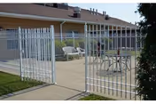 Small fenced outdoor patio with white metal chairs and a table in front of a single-story building.