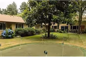 Outdoor putting green with three golf holes in front of a single-story building surrounded by trees and shrubs at Parkview Christian Retirement Community.