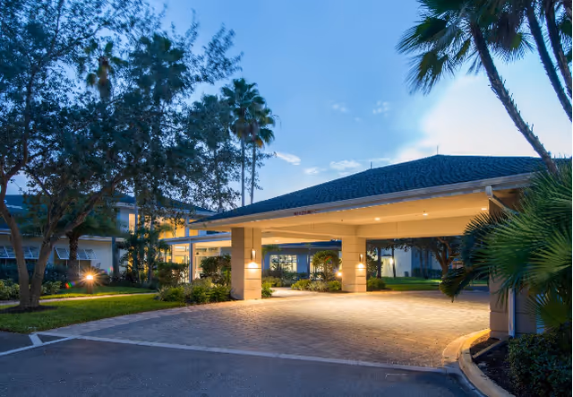 Entrance canopy of Aviva Senior Living with a drive-up lane and palm trees.
