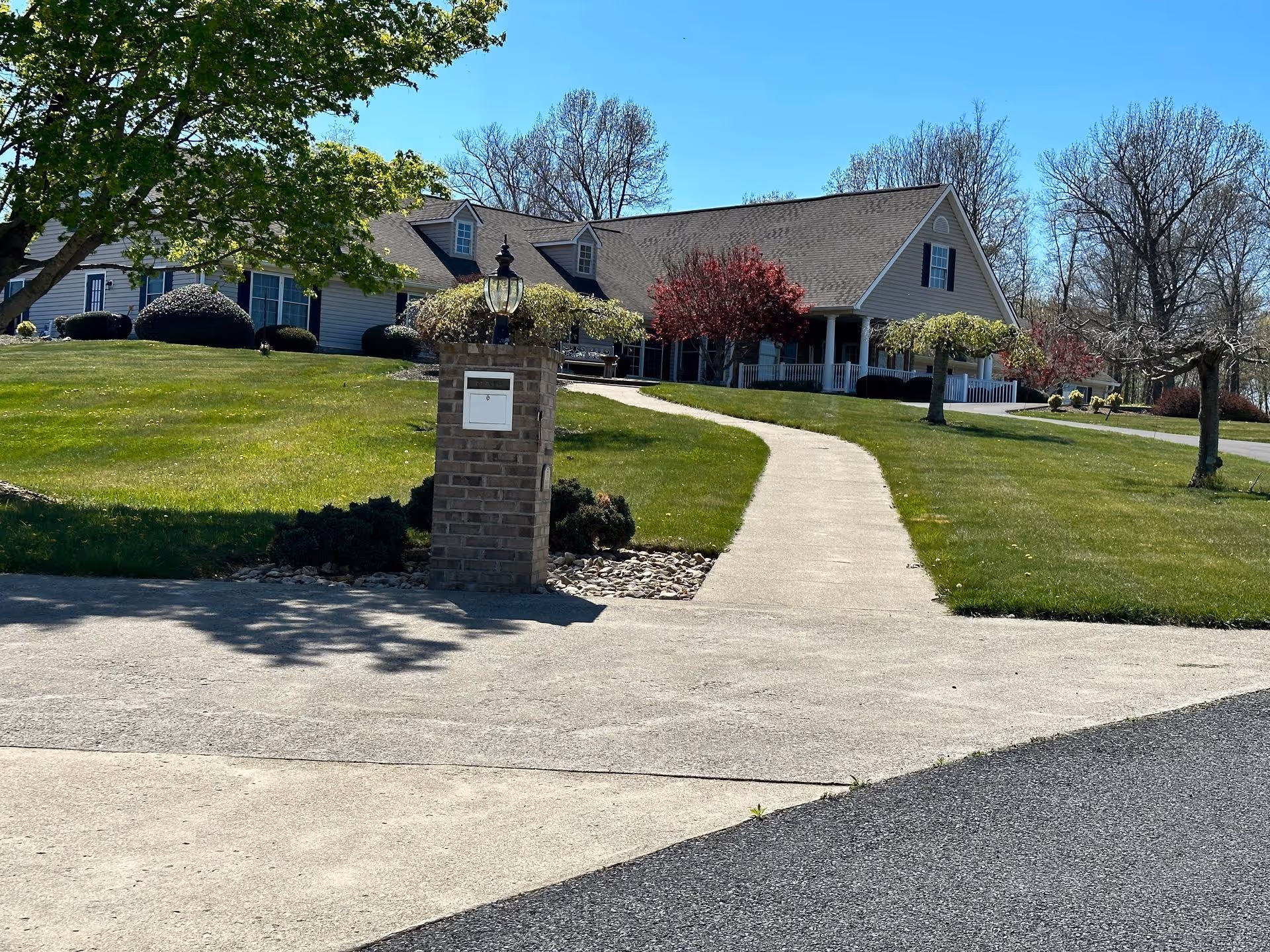 Front view of a single-story residential building with a curved concrete walkway, brick mailbox pillar, and landscaped lawn under a clear blue sky.