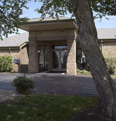 Front entrance of a brick senior living facility with a covered doorway and trees.