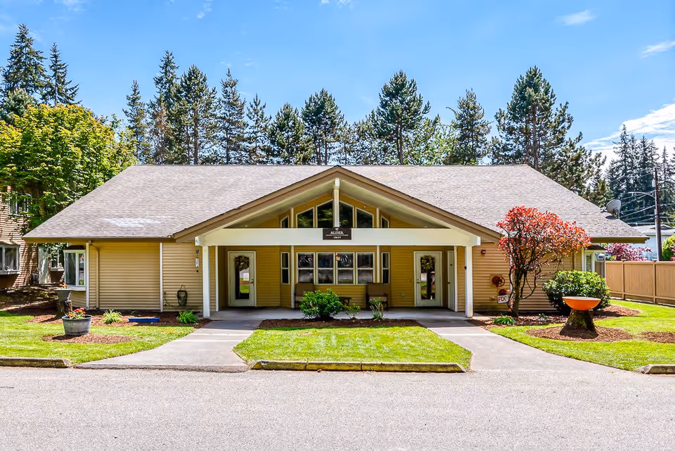Single-story yellow cottage-style building with a covered gabled entrance, manicured lawn, and landscaping.
