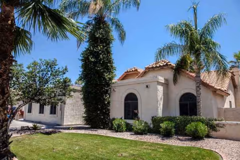 Cream-colored senior living facility exterior with palm trees and trimmed shrubs.