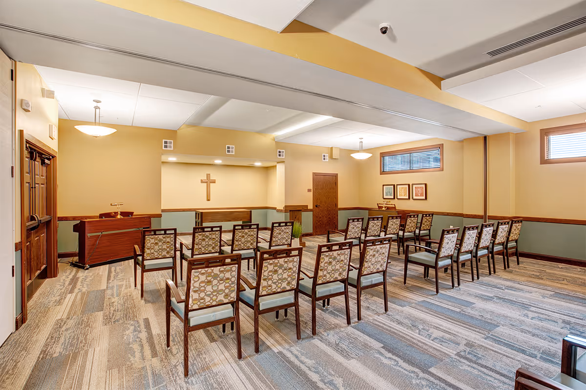 Chapel-style meeting room with rows of chairs facing a podium and a wall-mounted cross.