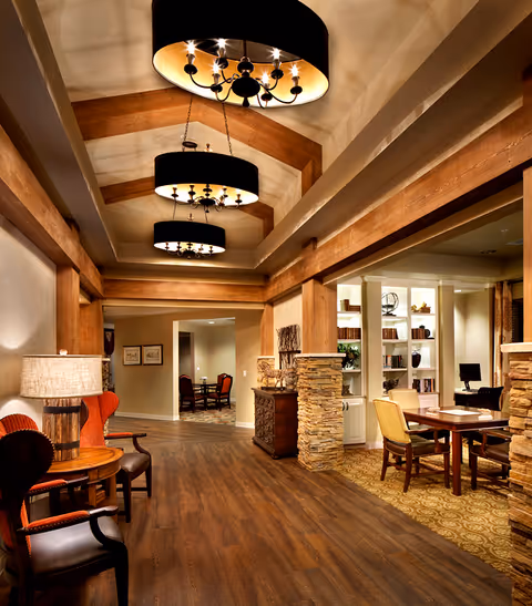 Warm wood-beamed common room with chandeliers, seating, tables and built-in bookshelves.