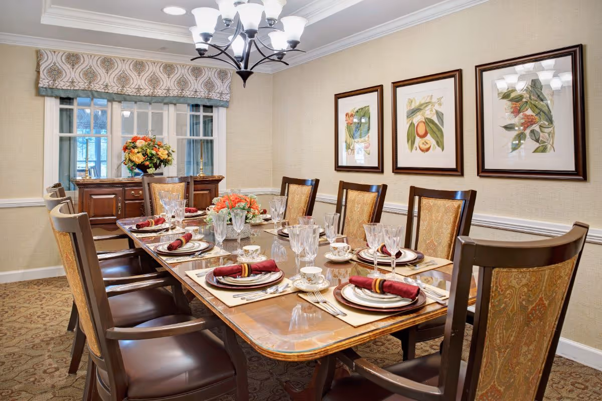 Formal dining room with a long set table for eight, upholstered chairs, a chandelier, floral centerpieces and framed botanical prints on the wall.