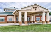 Front exterior view of Chateau Terrebonne Health Care building with a covered entrance supported by columns, a green roof, and a well-maintained lawn in front.
