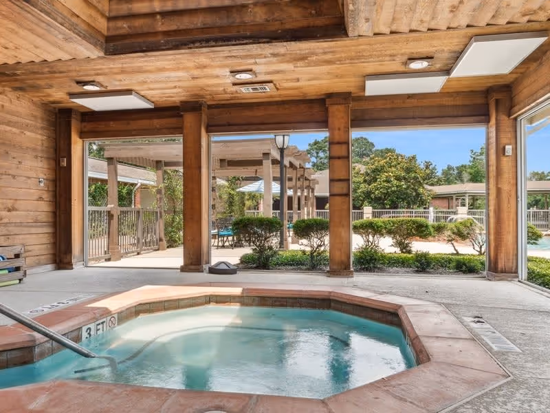 Covered indoor hot tub area with large open windows overlooking an outdoor pool and landscaped courtyard.