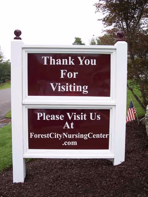 Outdoor white wooden sign with maroon panels reading Thank You For Visiting and ForestCityNursingCenter .com.