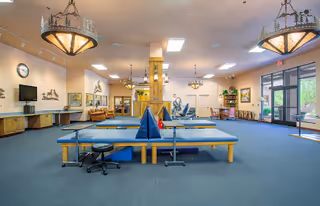 Spacious rehabilitation therapy room with treatment tables, exercise equipment, seating areas and large windows.
