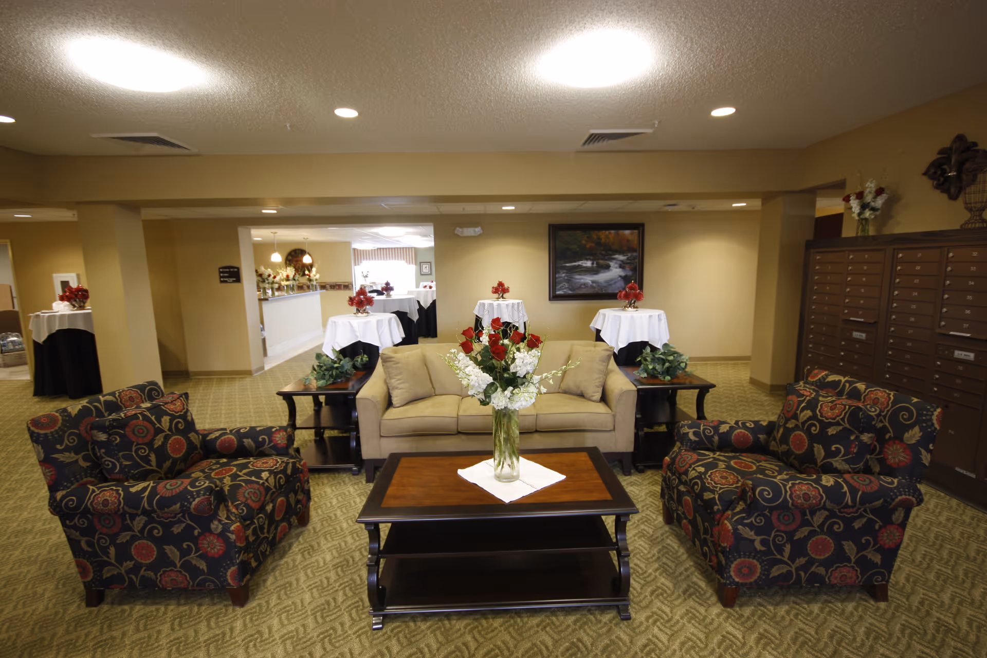 Lobby seating area with a sofa, two patterned armchairs and a coffee table topped with a vase of flowers.