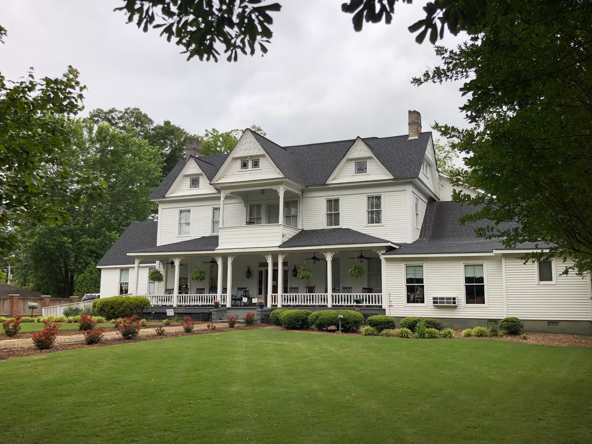 A large white two-story building with a wraparound porch and manicured lawn.