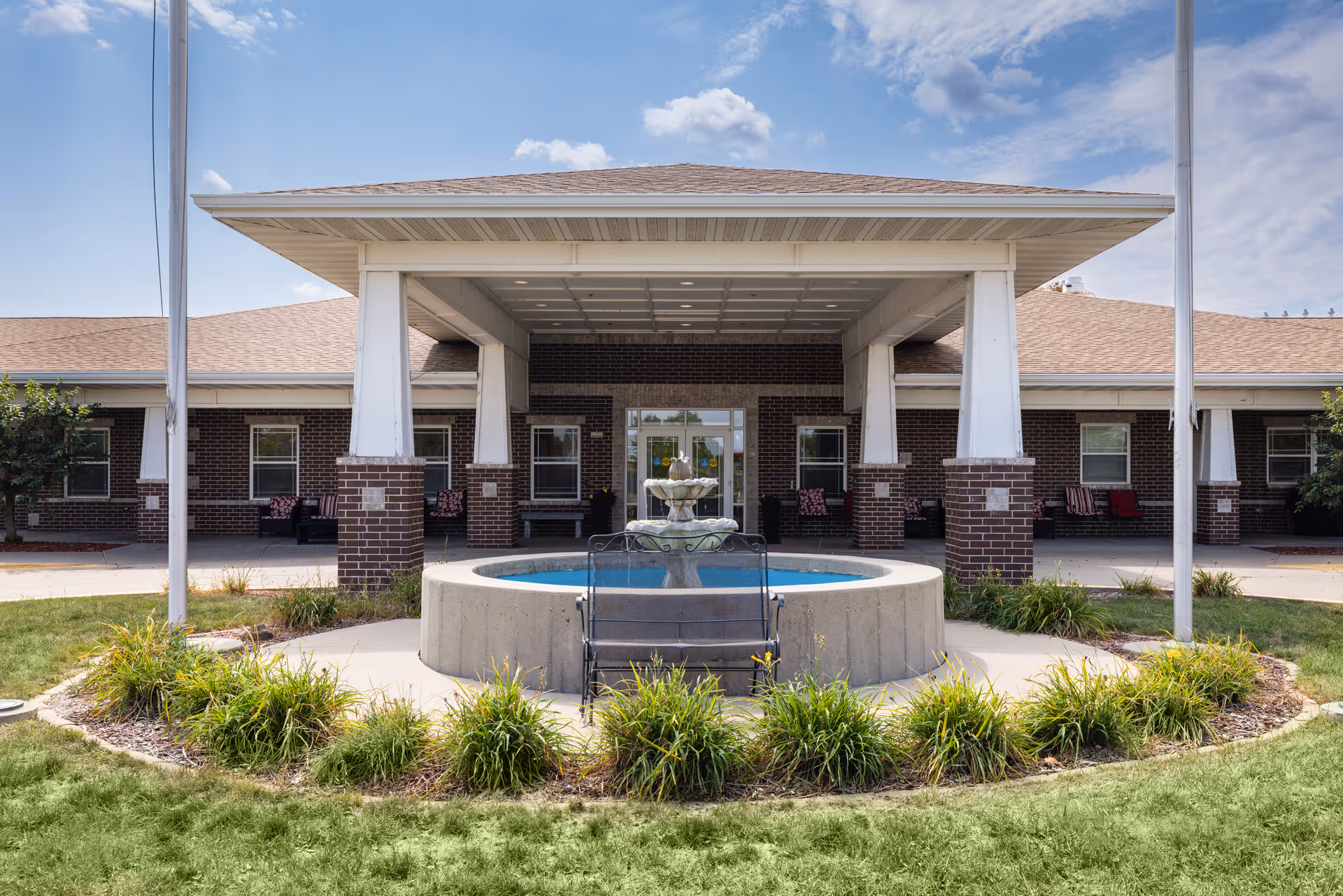 Front entrance of a senior living building with a covered porte-cochere and a circular fountain in the foreground.