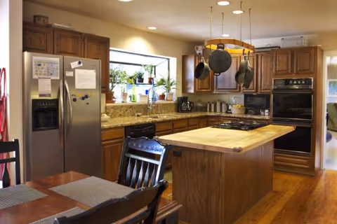 A warm wood kitchen with island, hanging pots, stainless appliances, and a dining table.