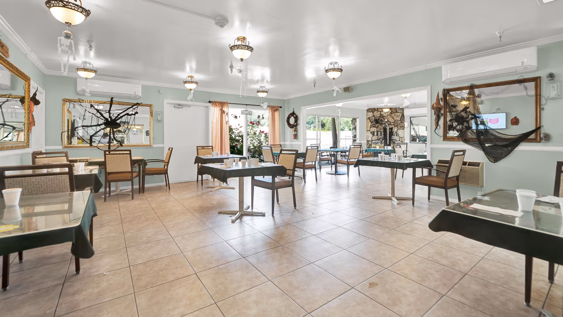 Spacious dining room with multiple tables and chairs, tiled floor, and decorative mirrors and wall hangings.