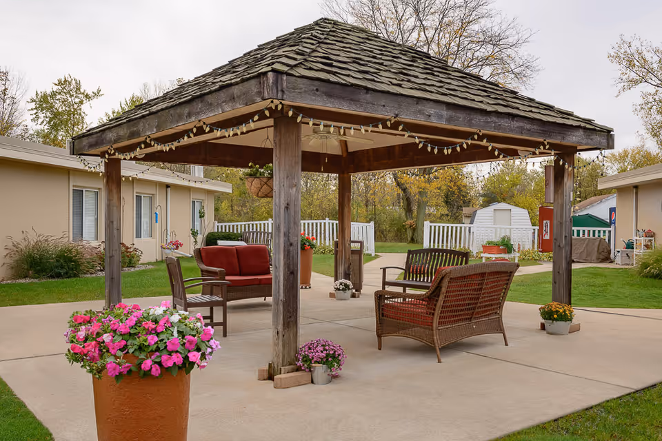 Wooden gazebo with outdoor seating and potted flowers in a courtyard.