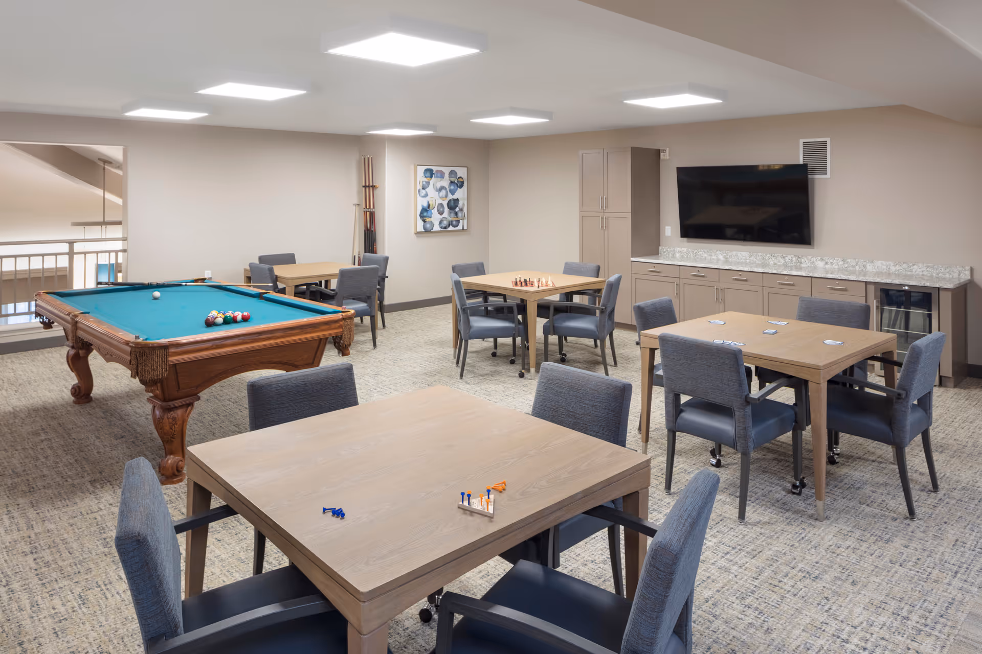 Community game room with a pool table, several tables and chairs, and a wall-mounted TV.