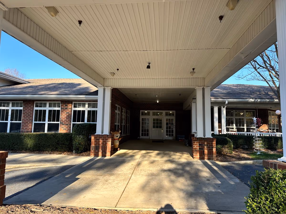 Covered porte-cochere entrance to a brick senior living building with white columns, windows, and double doors.