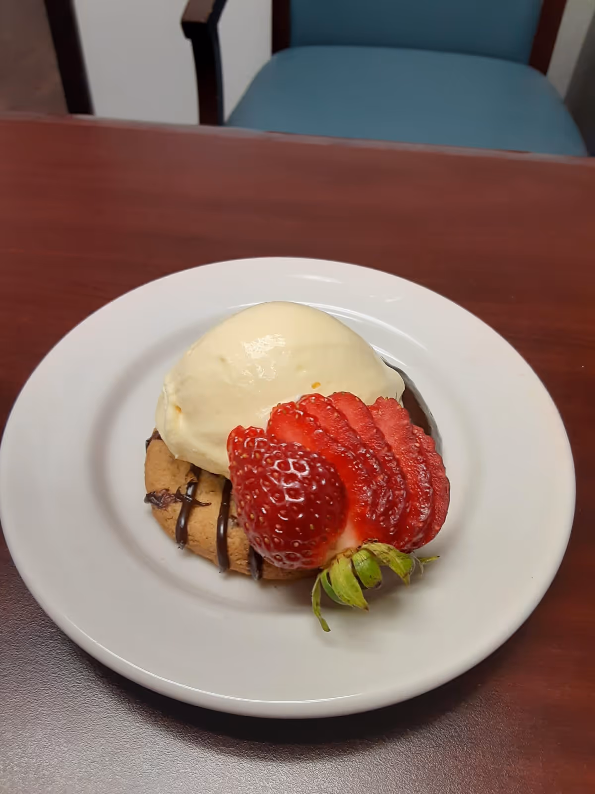 A dessert plate with a cookie topped by a scoop of vanilla ice cream and a sliced strawberry on a table.