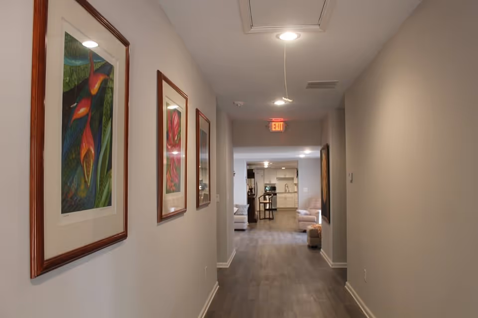 Long interior hallway with framed artwork on the left wall leading to a living area and kitchen at the far end.