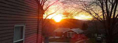Sunset over neighboring houses and trees beside a red-siding senior care home.