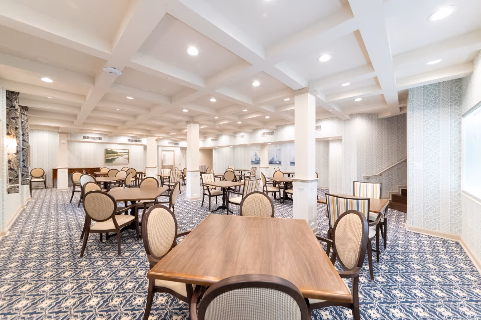 Spacious dining room with multiple wooden tables and upholstered chairs under a coffered ceiling.