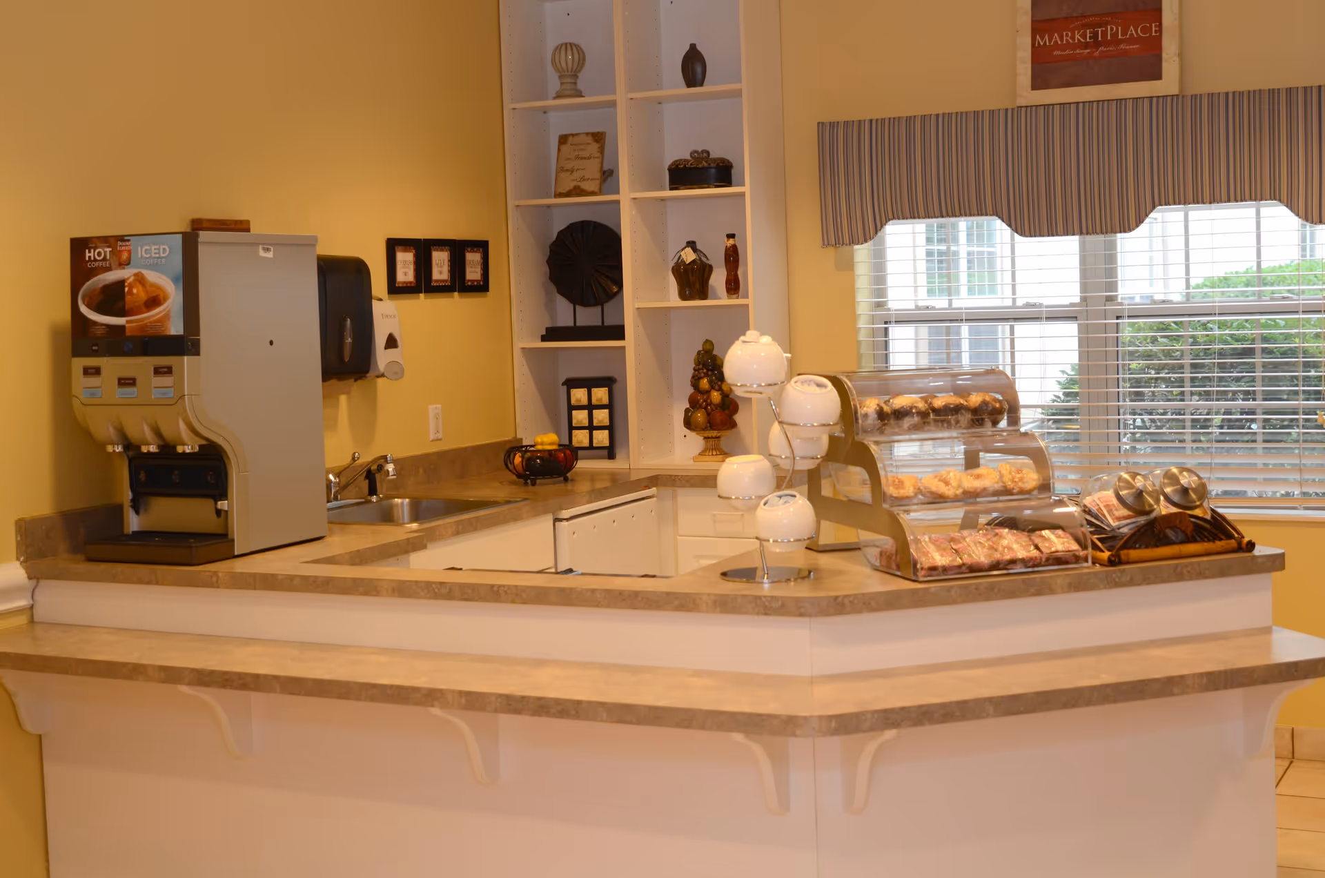A serving counter with a coffee machine, pastry displays, decorative shelving, and a window behind.