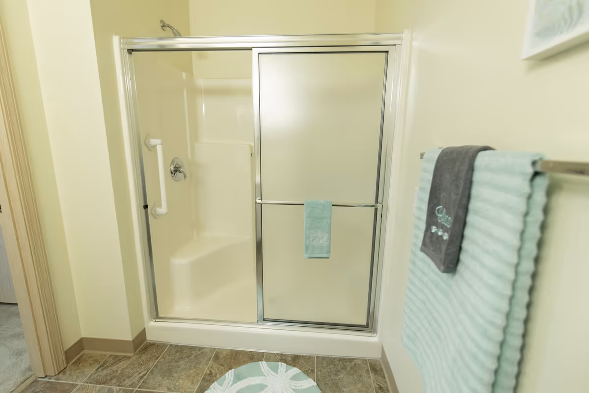 Frosted sliding shower enclosure in a bathroom with mint and gray towels on a nearby towel rack.