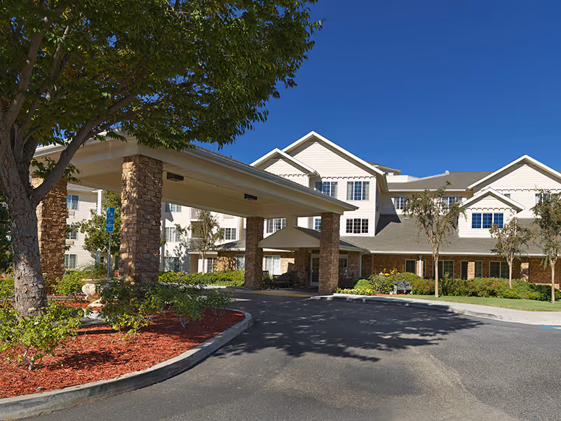 Sunny exterior view of Holiday Golden Oaks senior living facility with stone entrance pillars and canopy.