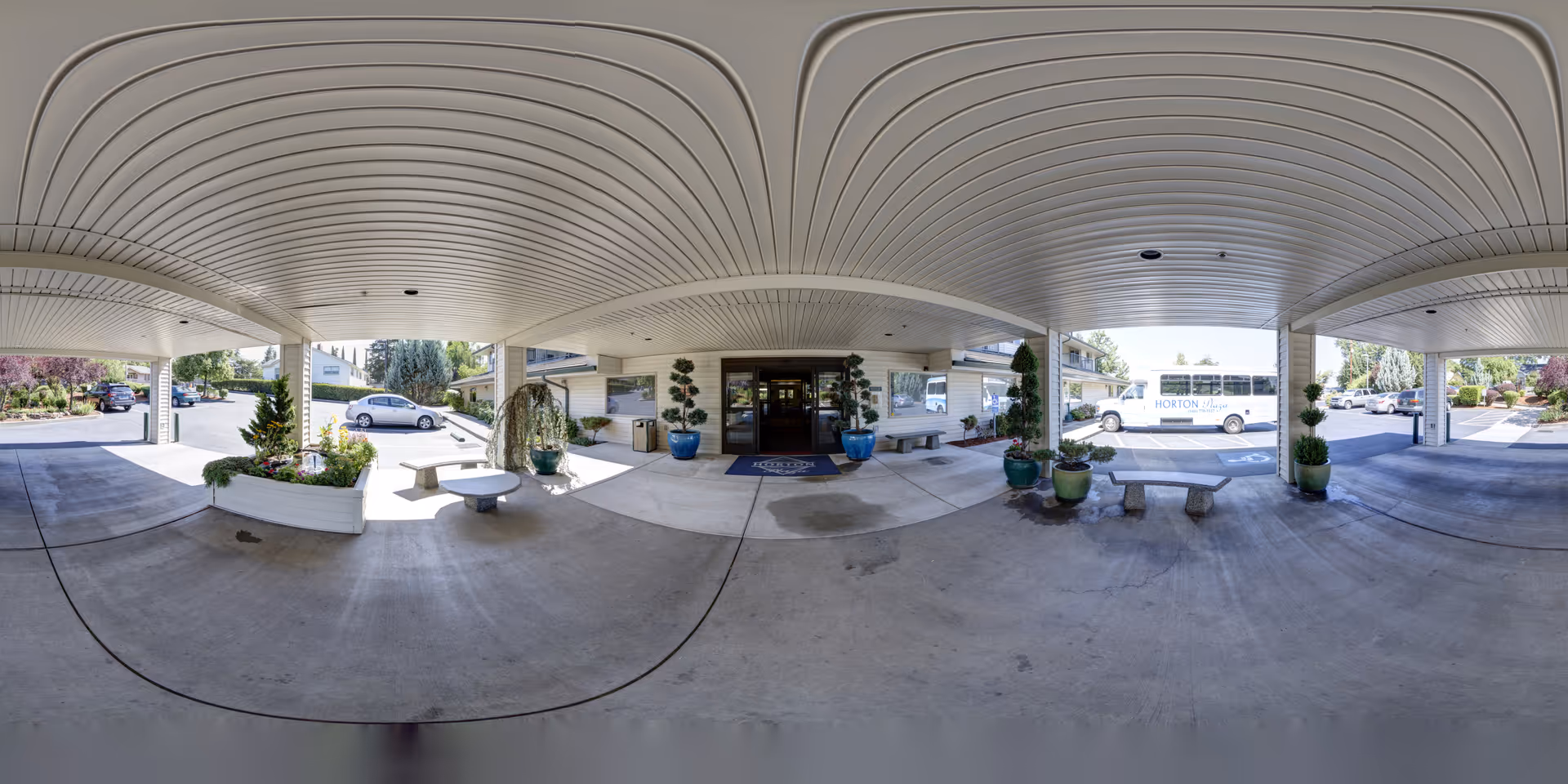 Covered drive-through entry with potted plants, benches, and a shuttle bus at the front of the Horton Plaza facility.