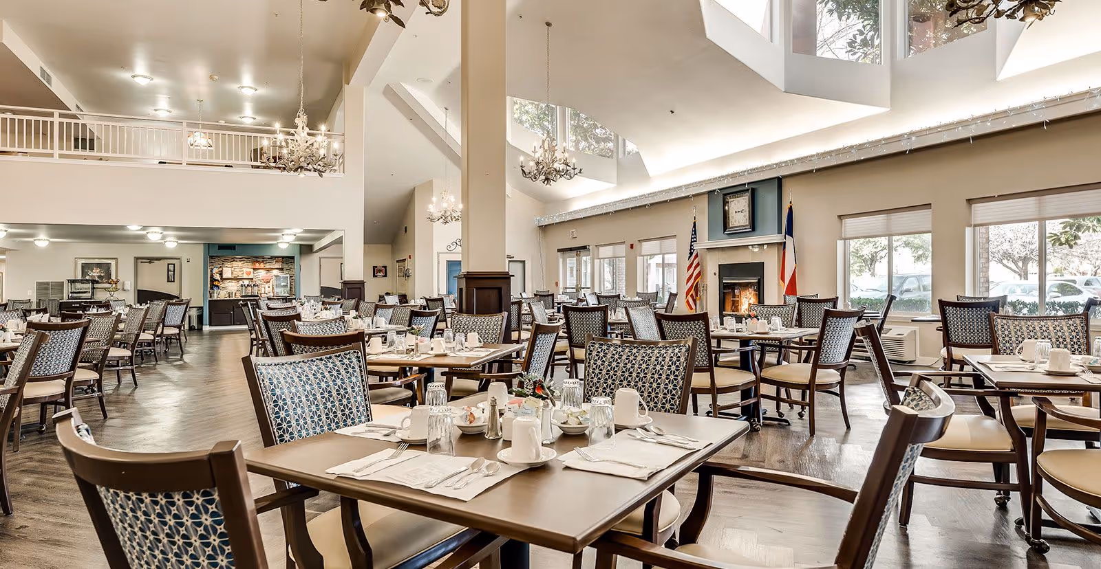 Bright, open dining room with many set tables and chairs, chandeliers, skylights, and a fireplace.