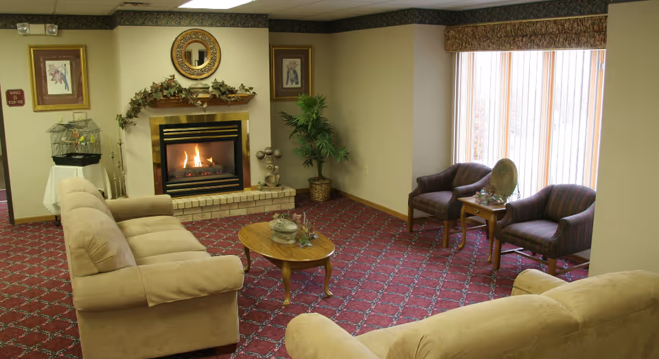 Cozy senior living room with sofas, a fireplace, coffee table, armchairs, and large windows.