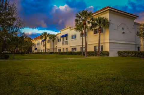 Exterior view of Banyan Place senior living building with palm trees and lawn.