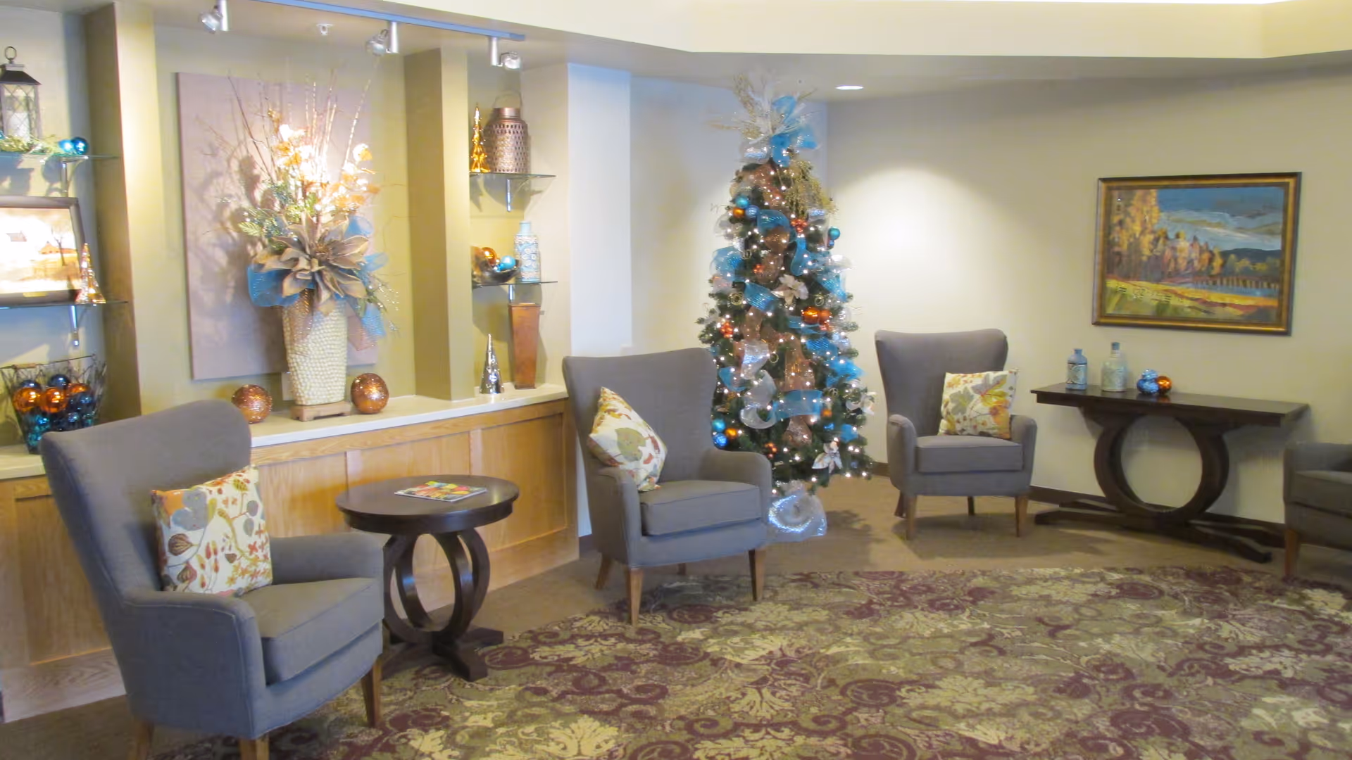 A decorated common seating area with upholstered armchairs, side tables, and a Christmas tree.