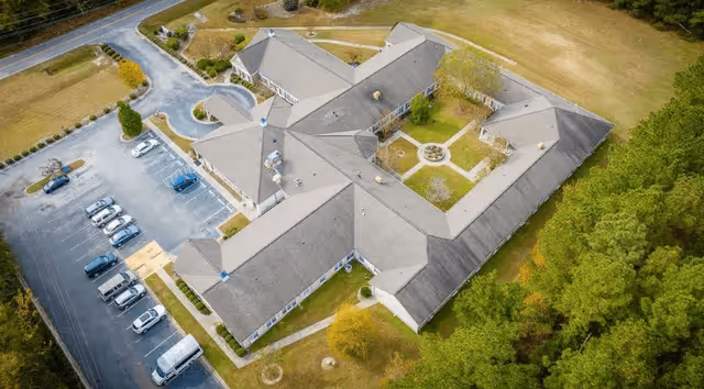 Aerial view of The Legacy of Orangeburg senior living facility showing a large building with a central courtyard, surrounded by parking spaces and greenery.