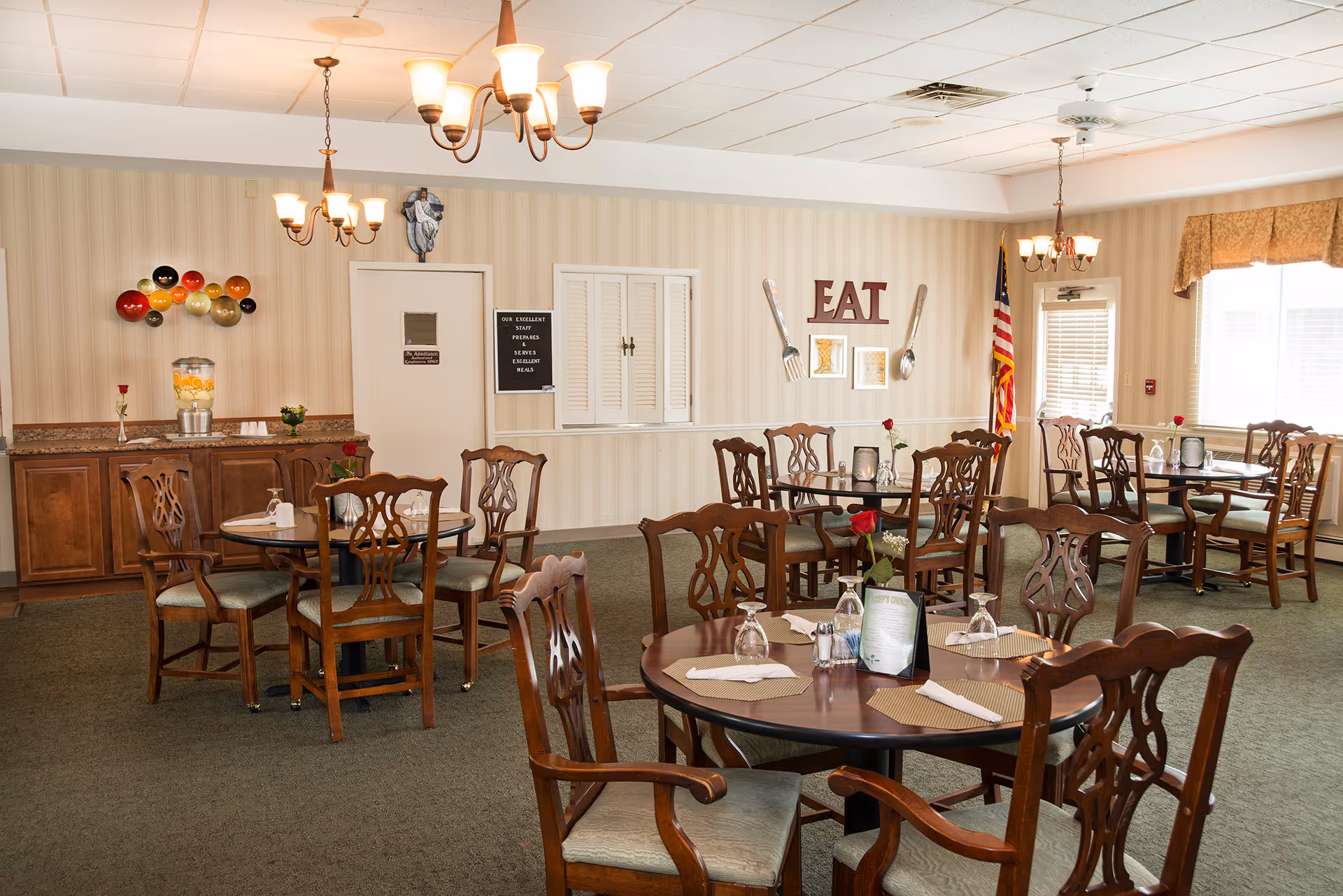 Dining room with round wooden tables and chairs, chandeliers, and a wall sign that reads "EAT".