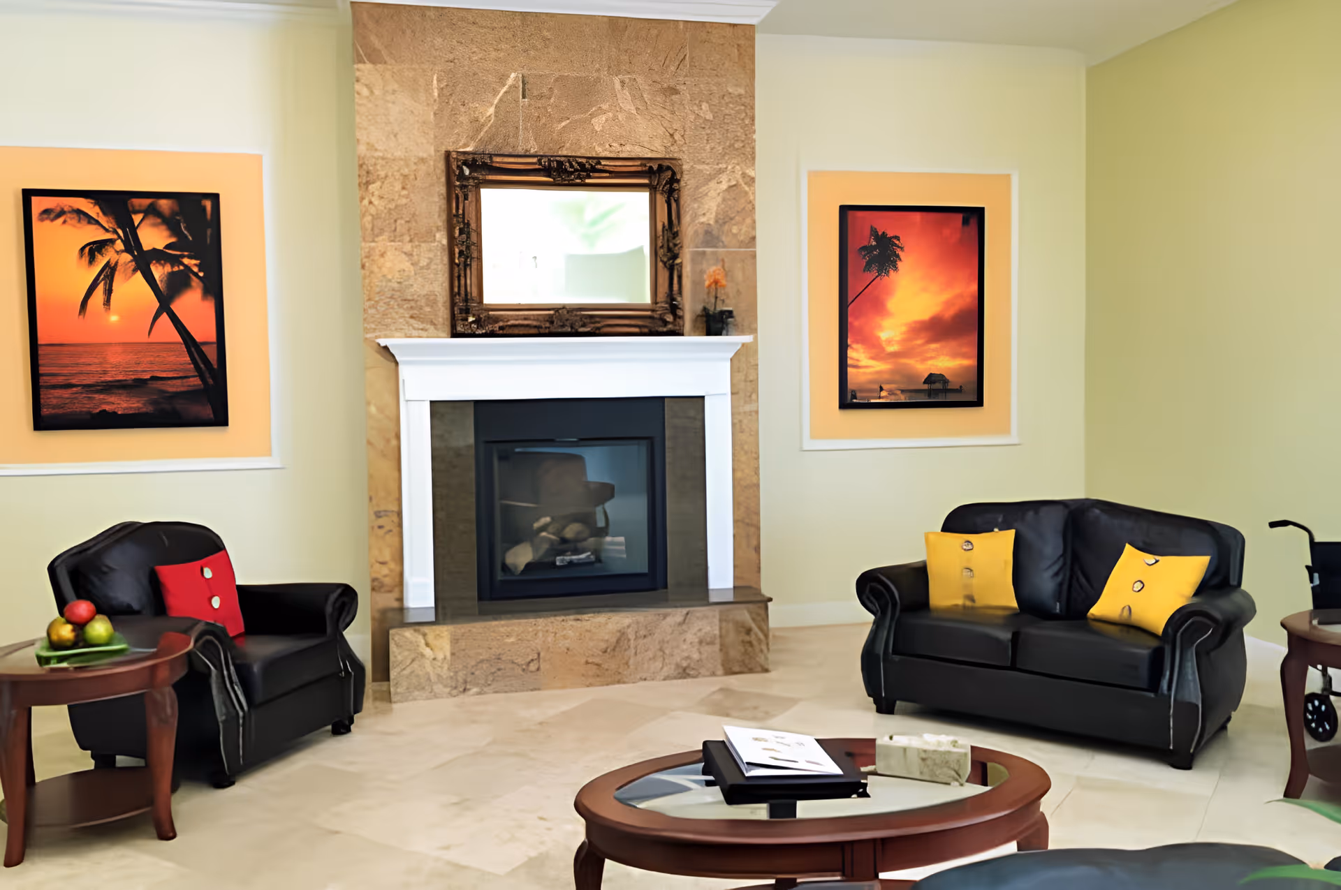 Bright living room with a central fireplace, black leather seating, a round coffee table and sunset artwork on the walls.