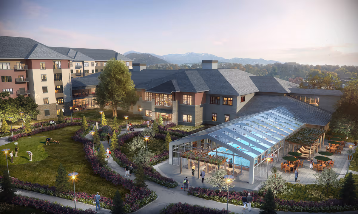 A senior living facility named Summit Vista featuring a large building with multiple floors, a glass-enclosed indoor swimming pool, outdoor patio seating with tables and umbrellas, landscaped gardens with walking paths, and people enjoying various activities such as walking and playing with dogs. The scene is set during dusk with mountains visible in the background.