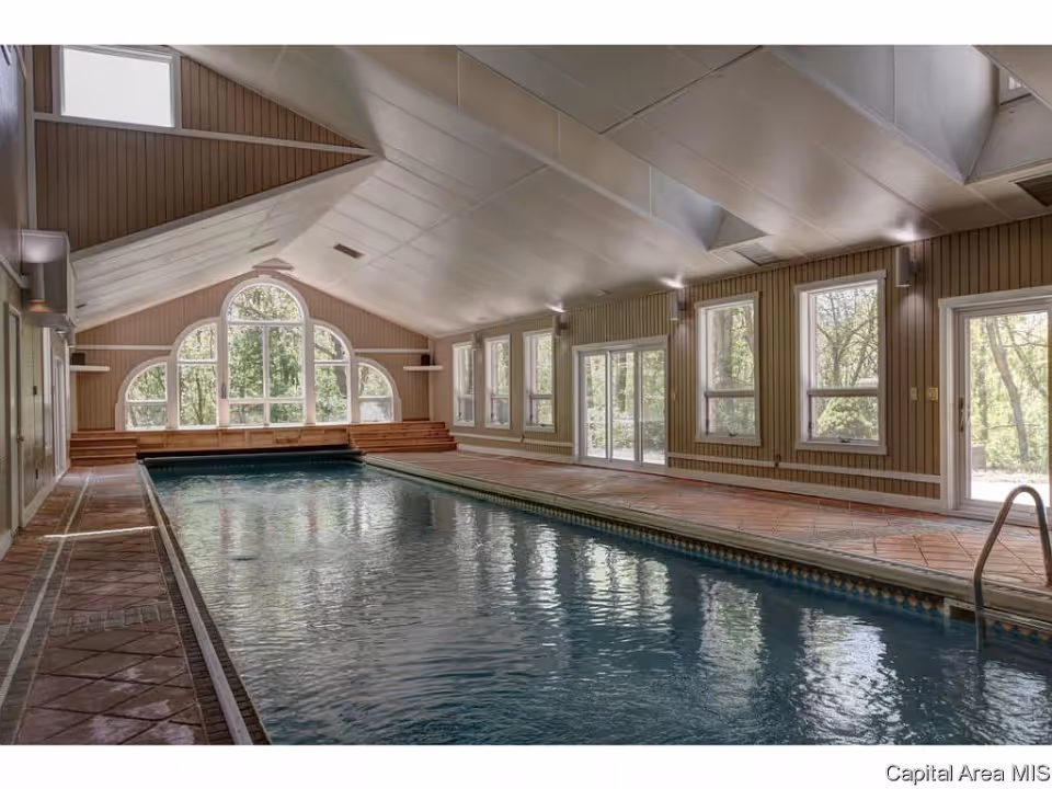 Indoor community swimming pool with a vaulted ceiling, large arched windows and tile decking.
