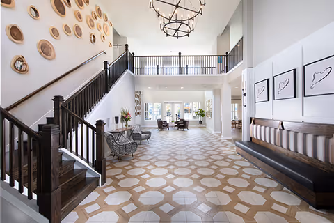 Spacious, well-lit lobby with patterned tile floor, dark wood staircase, seating areas, chandelier, and decorative wall art.