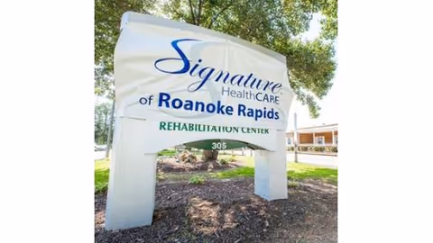 Outdoor sign for Signature HealthCARE of Roanoke Rapids Rehabilitation Center with trees and a building in the background.