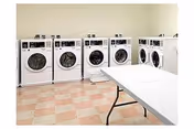 Row of washing machines along a tiled laundry room with a folding table.