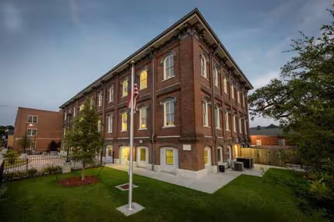 Front exterior of The Suites at Algiers Point, brick building with flagpole and green lawn.